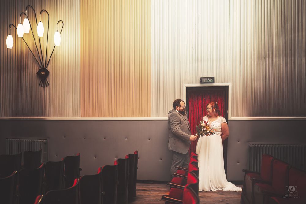 Bride and groom exchange vows in a vintage wedding venue with red curtains and warm lighting.