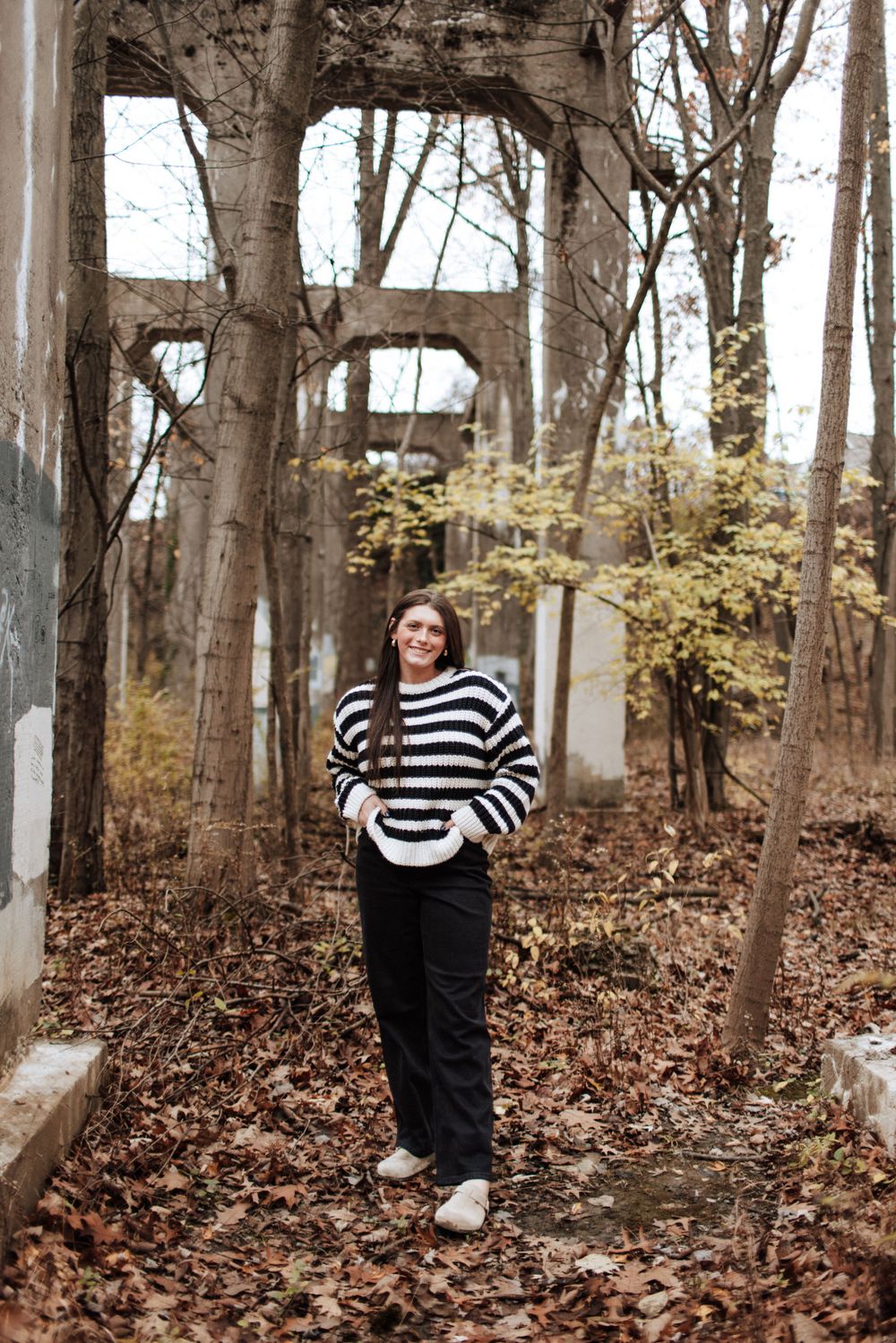 Smiling brunette teen girl in striped sweater poses among autumn ruins outdoors.