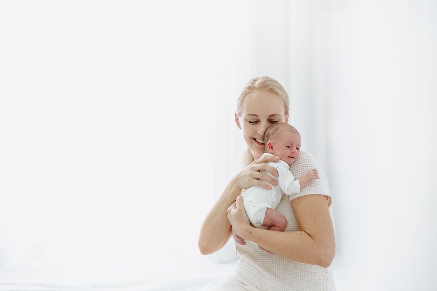 A loving mother gently holds her newborn baby in her arms against a bright white background.