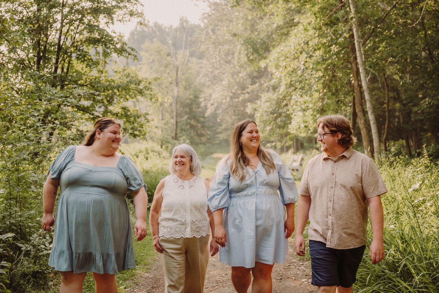 Four people walking together on a forest path surrounded by lush green trees, smiling and holding hands.