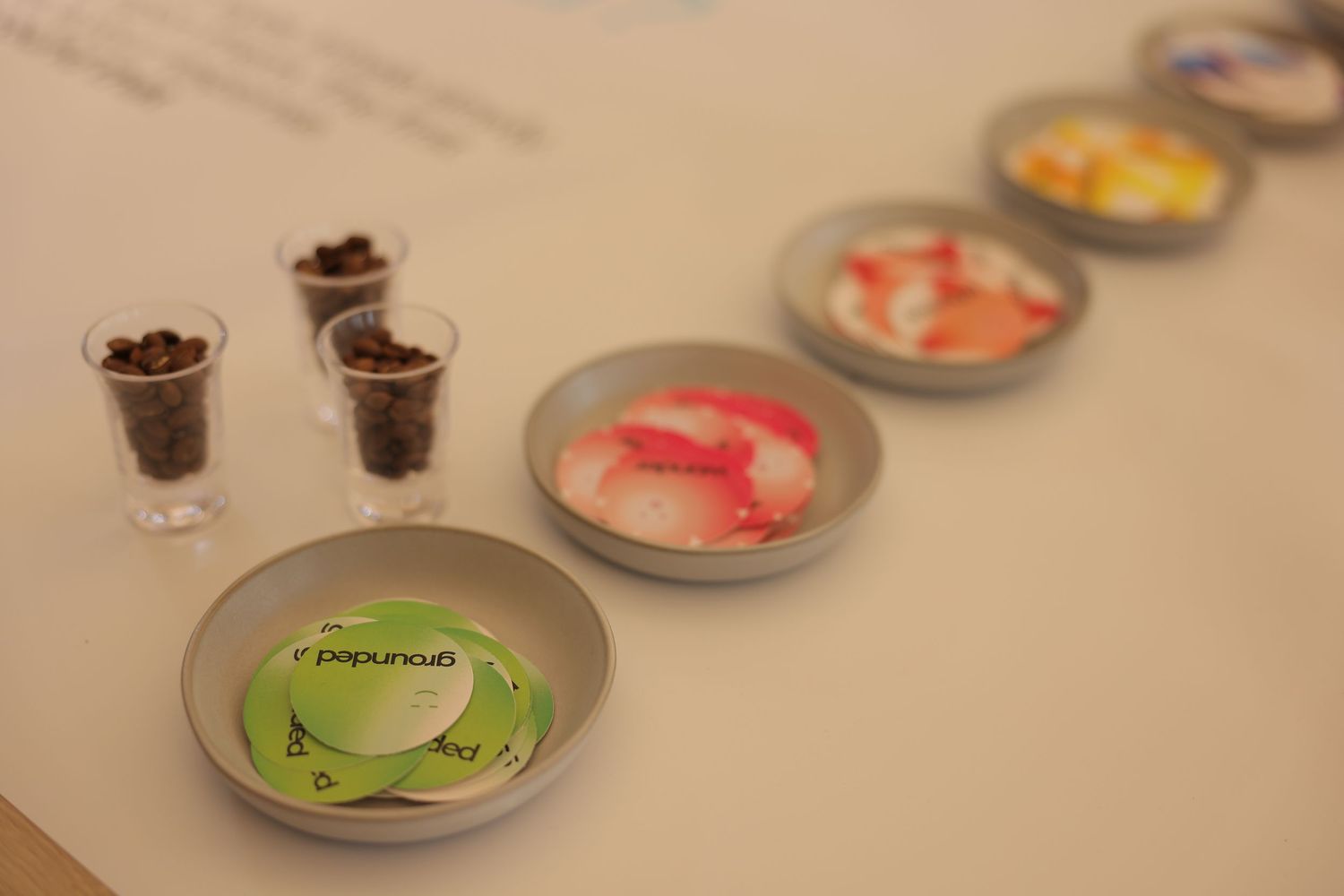 Gray dishes and glass cups displaying colorful branded candies and chocolate pieces arranged in a row on a white surface.