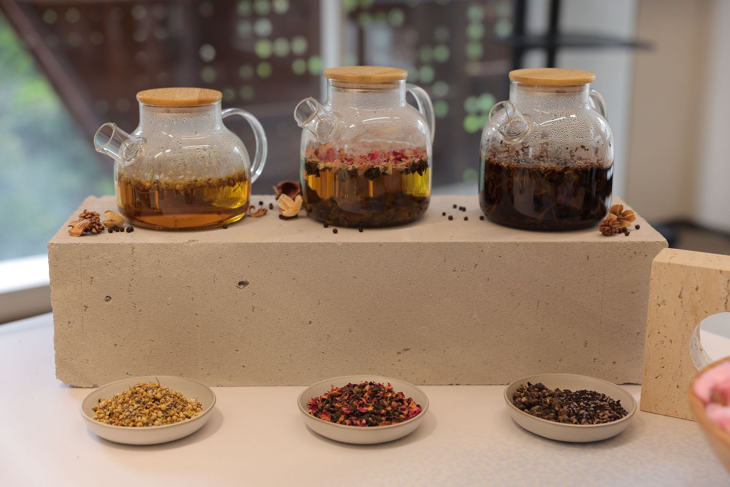 Three glass jars with wooden lids filled with infused oils on a stone tray, with spice bowls in front.