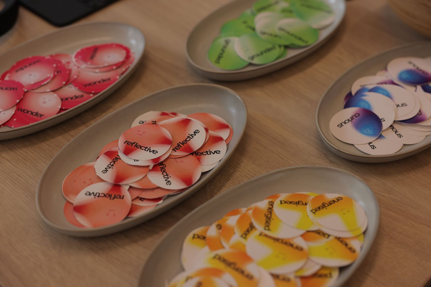 Oval gray dishes filled with colorful branded candy wafers in pink, green, white, and orange varieties on a wooden table.