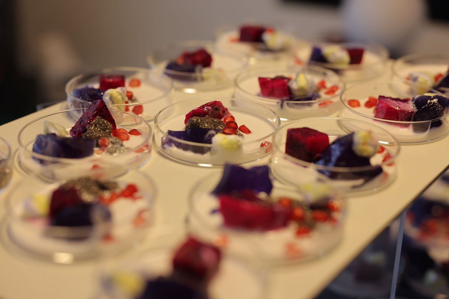 Elegant dessert appetizers in clear glass dishes with colorful purple and red garnishes arranged on a white tray.