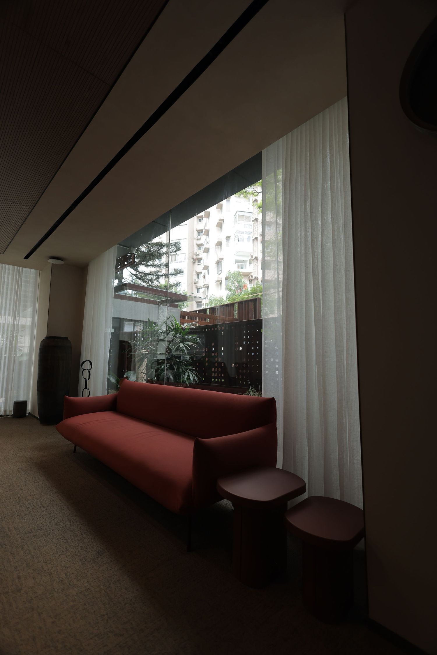 Modern red sofa with side tables by a large window with sheer white curtains in a contemporary hotel lobby.