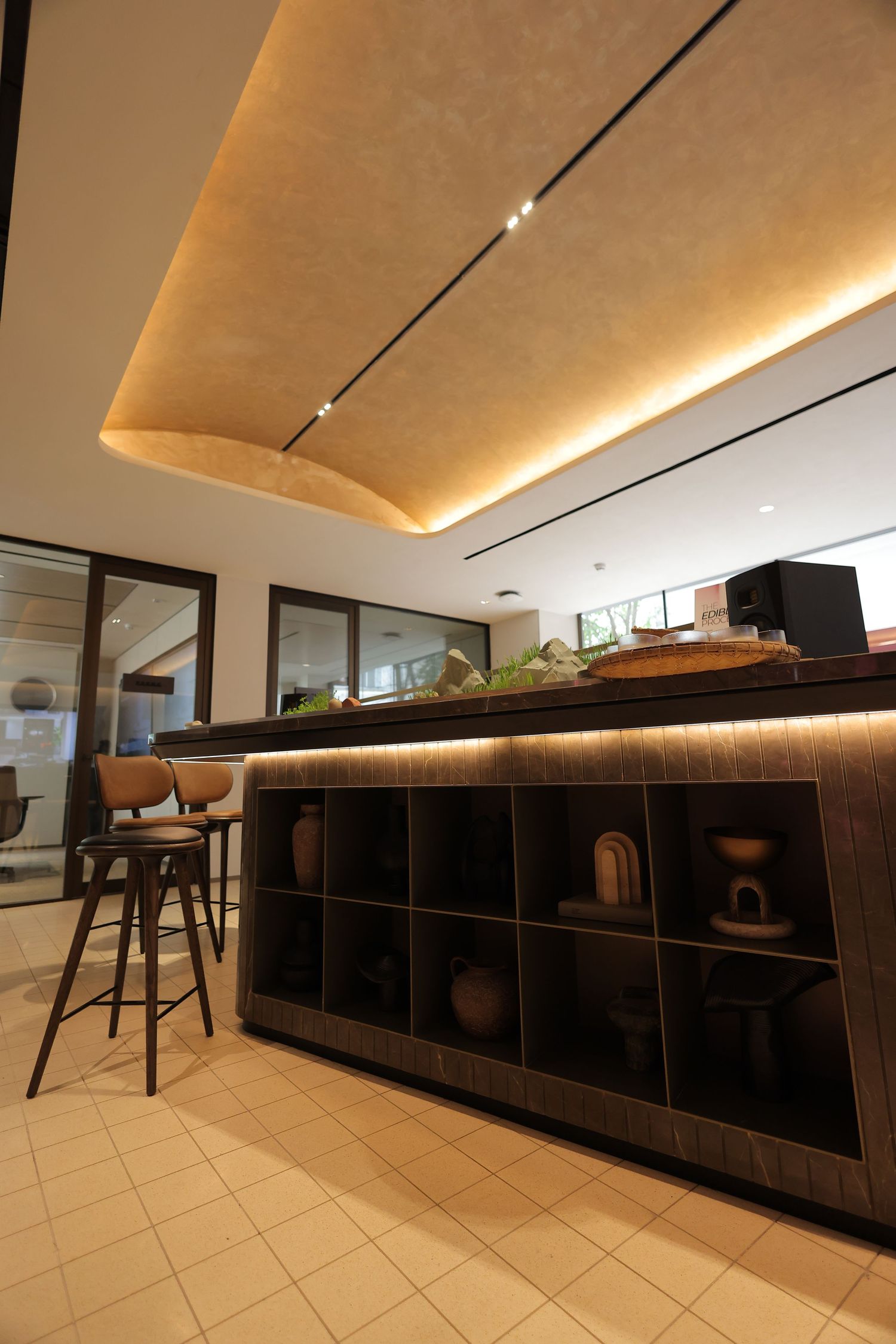 Modern interior bar counter with warm LED lighting, decorative pottery shelves, and bar stools in an elegant contemporary space.