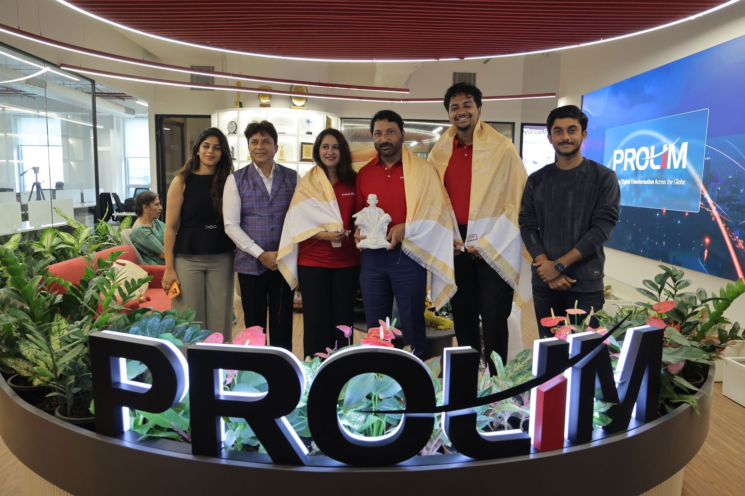 Group of young professionals posing together at PROLIM office lobby with branded signage and modern decor.