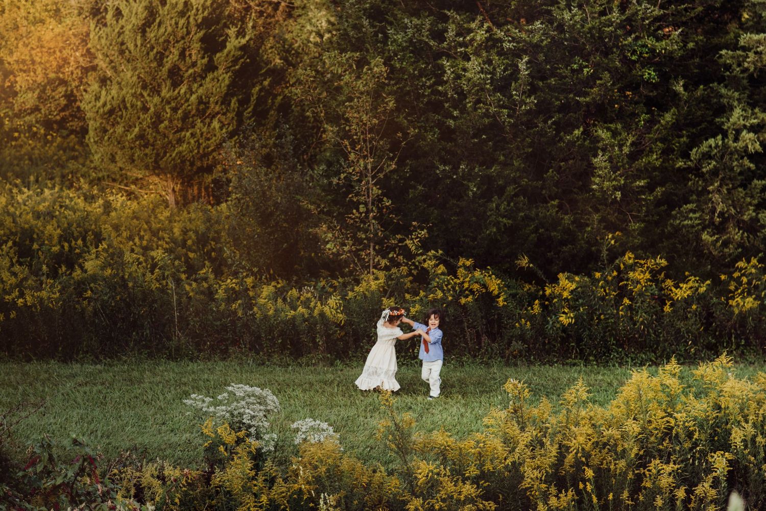 A young girl in a white dress stands by a sunlit riverbank, bathed in golden hour light.