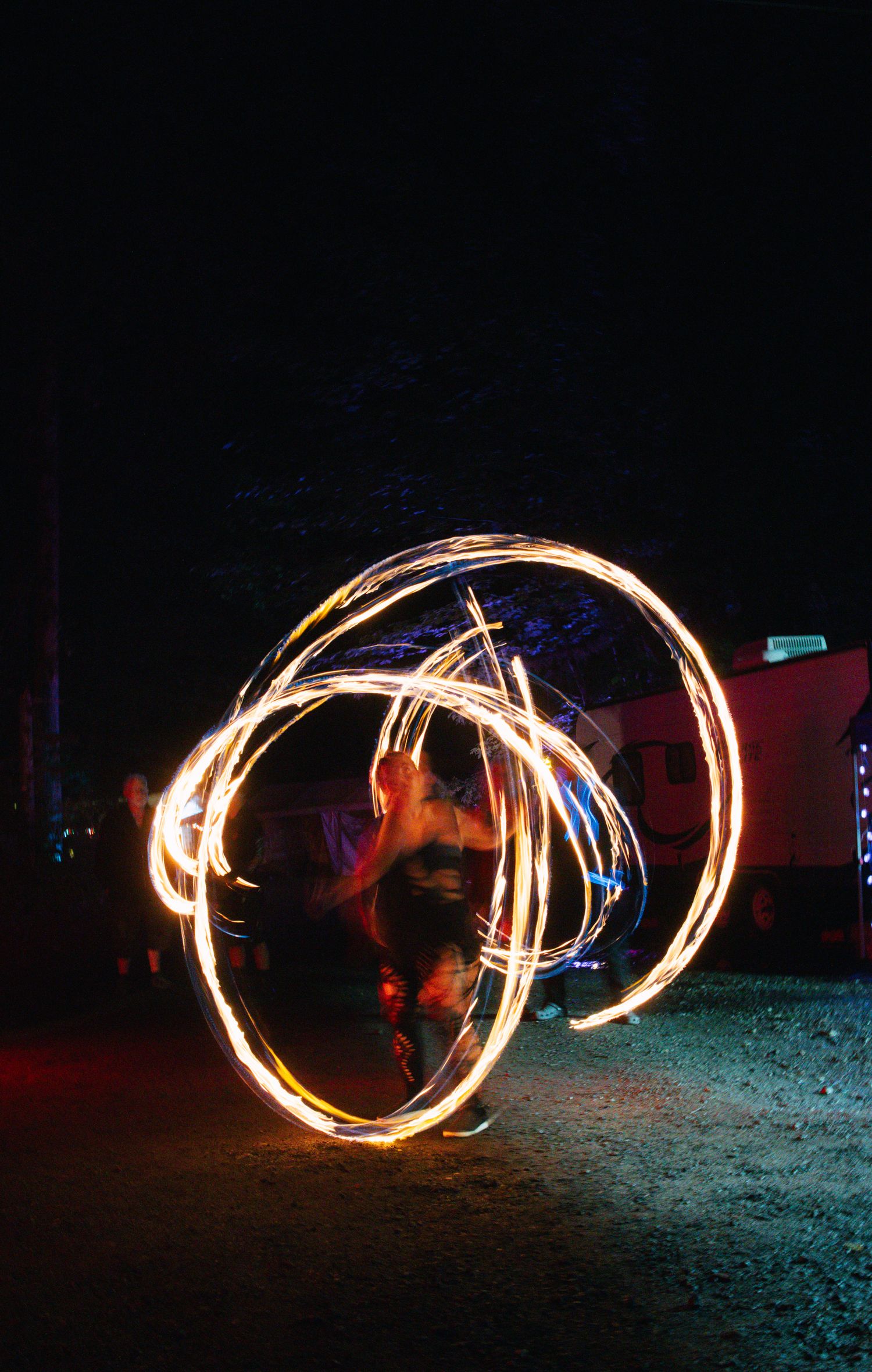 Fire performer spinning glowing poi at night creating circular light trails in a long exposure photograph.