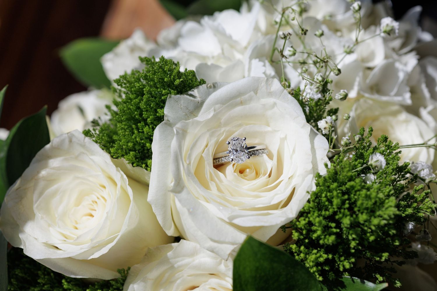 Diamond engagement ring nestled among white roses and greenery in an elegant bridal bouquet.