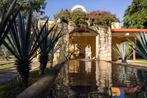 Couple standing under a stone arch beside a reflective pool, surrounded by agave plants at a Mexican hacienda.