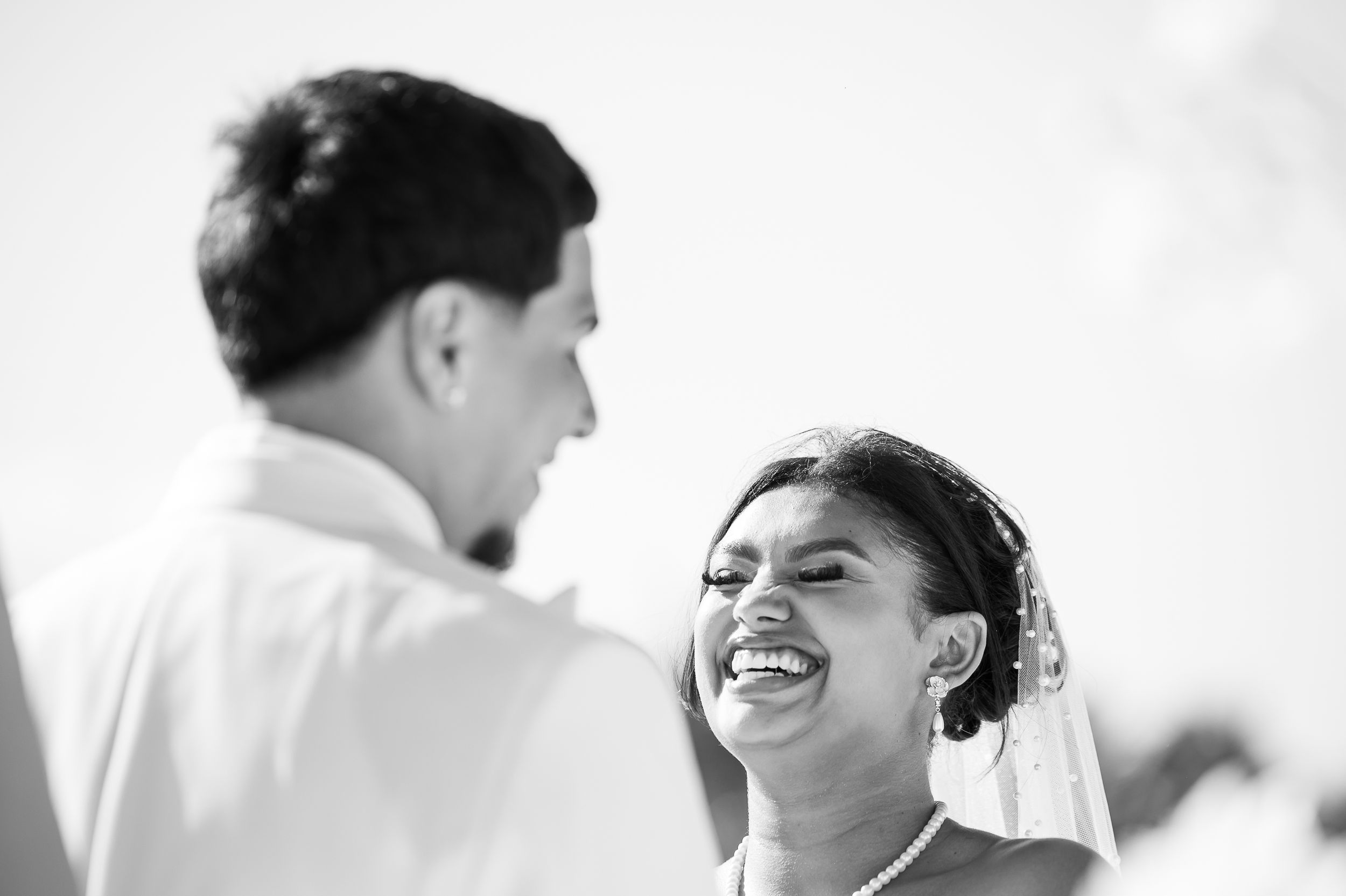 Black and white photo of a bride laughing joyfully with groom during outdoor wedding ceremony.