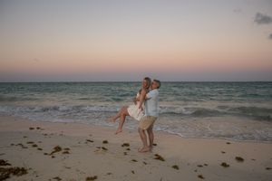 Couple embracing on a sandy beach at sunset with turquoise ocean waves in the background.