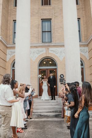Newlywed couple exits historic brick church as guests celebrate their wedding ceremony outdoors.