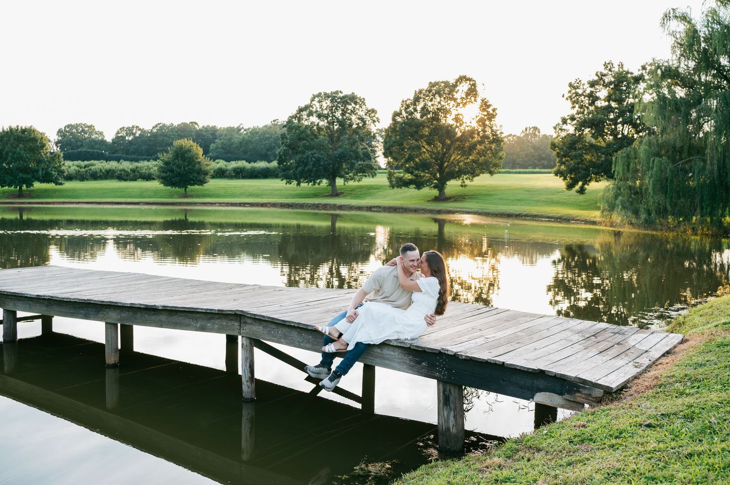 Couple sitting together on a lush green hillside field during golden hour sunset photography session in North Carolina
