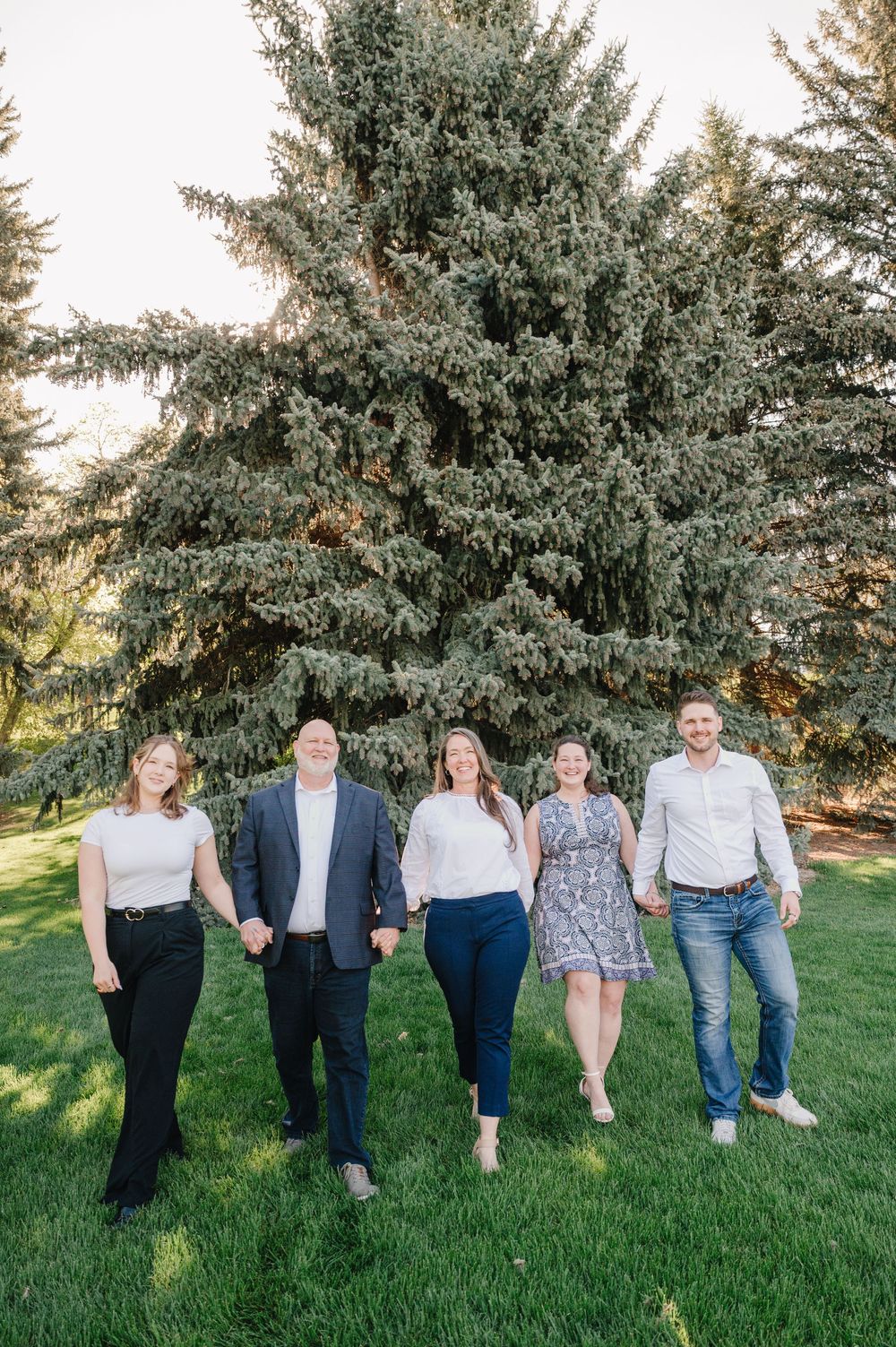 A group of people standing together on grass with large evergreen trees in the background.