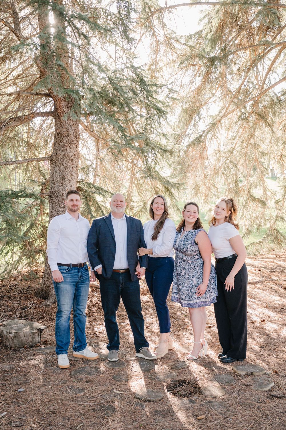 A group of people standing together in a forest setting with sunlight filtering through pine trees.