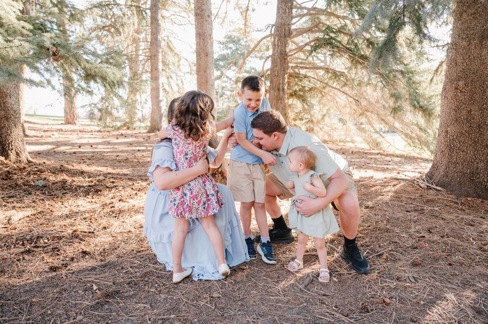 Family with young children sharing a joyful moment among pine trees in soft natural light.