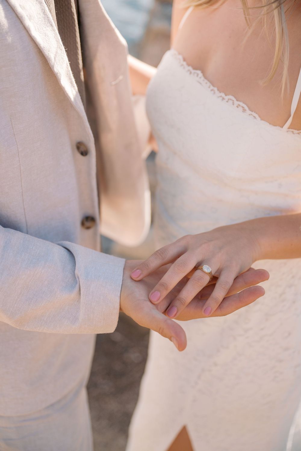 Close-up of bride and groom holding hands showing diamond engagement ring at outdoor wedding ceremony.
