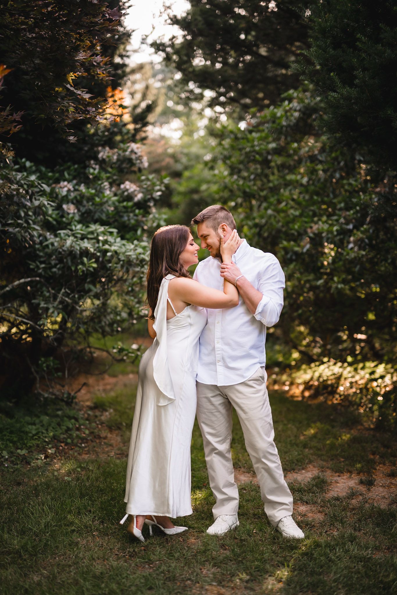 Couple in white outfits sharing a romantic moment in a lush green garden setting.