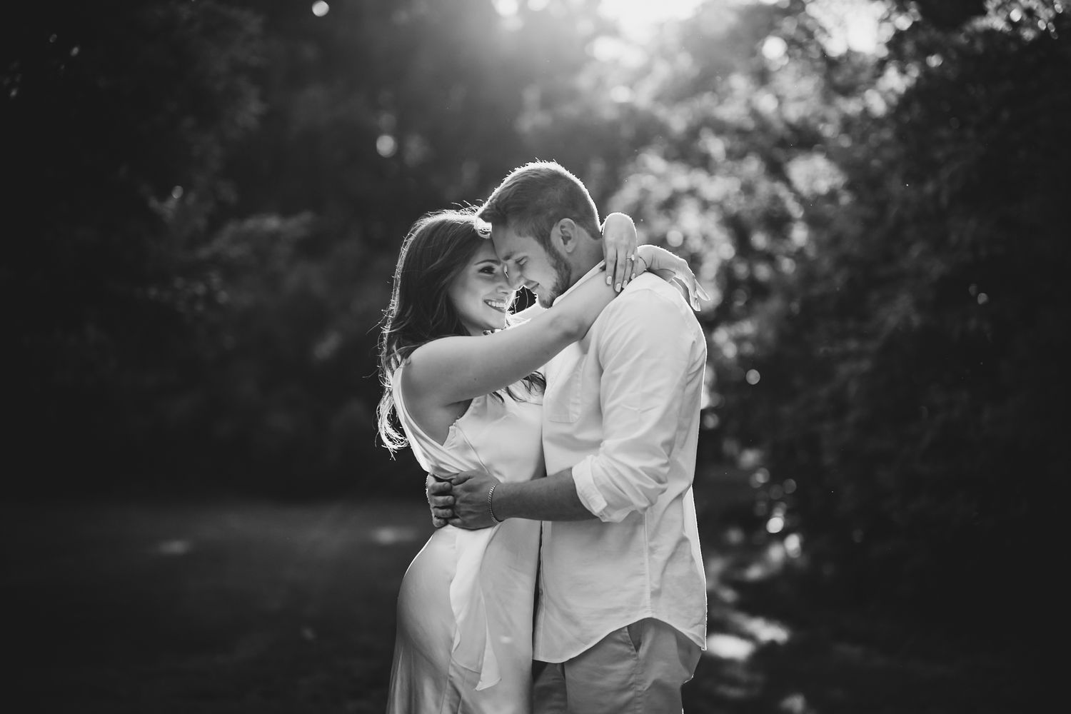 Black and white photo of couple hugging tenderly in a sunlit garden setting.