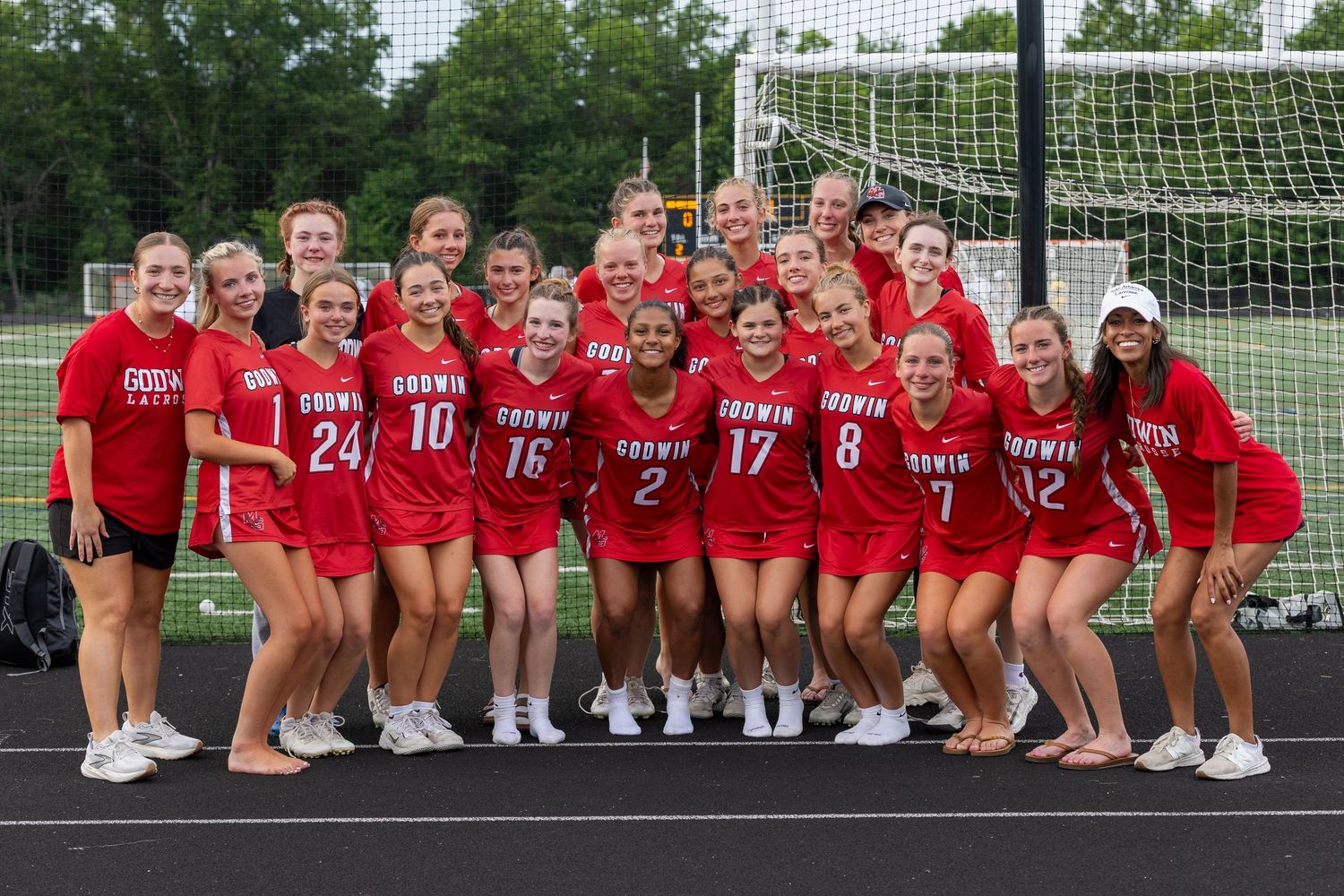 Godwin girls soccer team poses together in red uniforms on a green turf field in front of a goal net.
