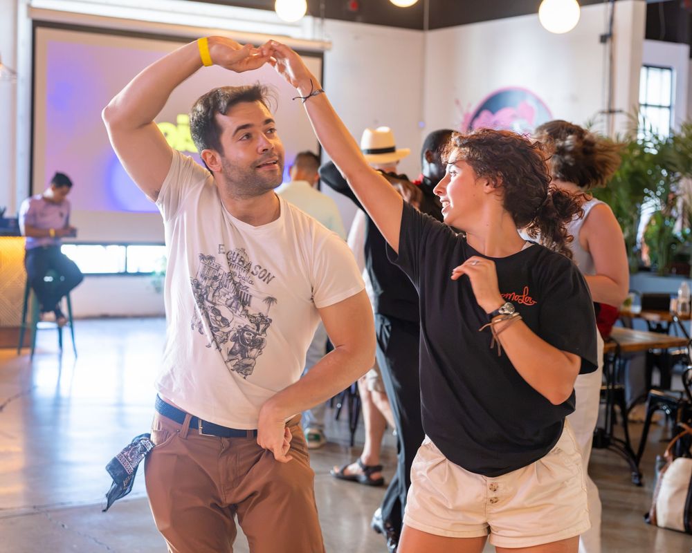A man and woman dancing together at an indoor social dance event, smiling and holding hands on the dance floor.