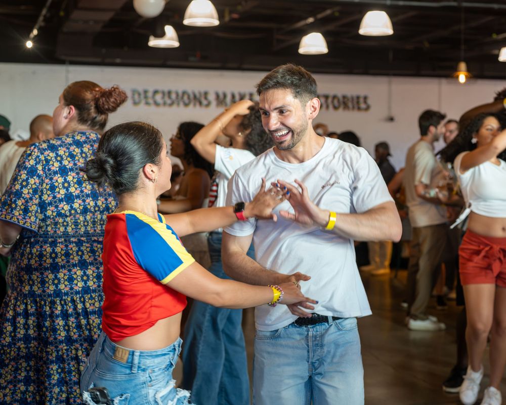 Two people dancing together at a lively indoor social event, smiling and holding hands on the dance floor.