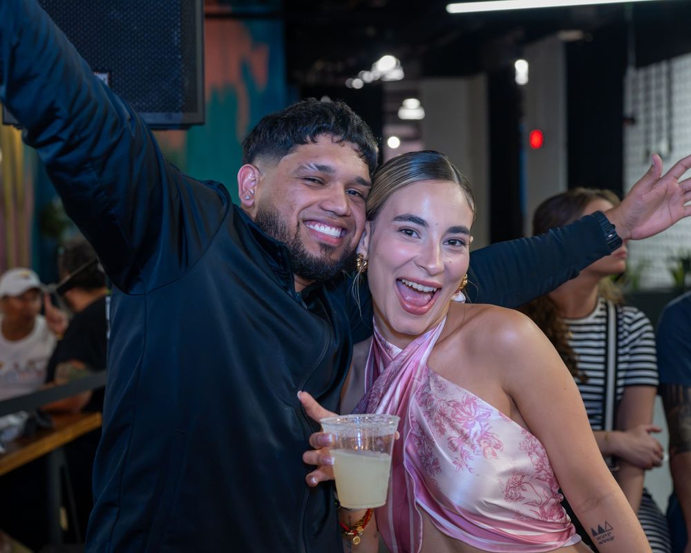 Excited couple poses together smiling at a lively party, woman holding a cocktail drink.