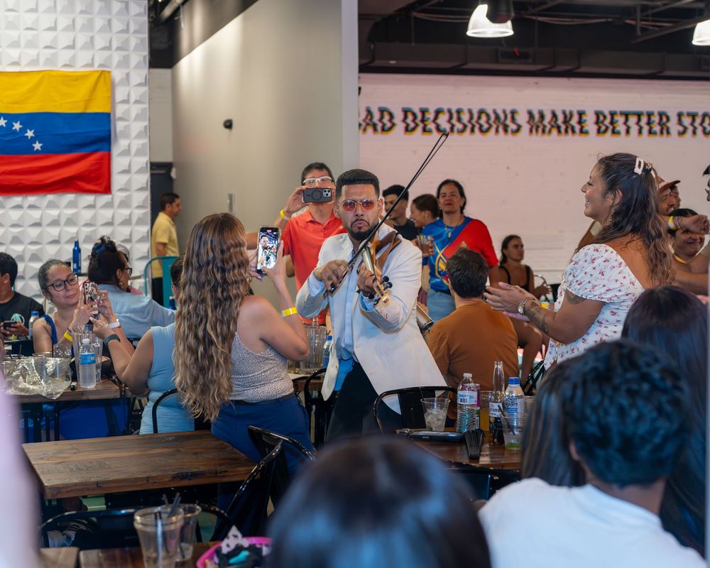 Violinist performs at lively Venezuelan cultural event with flag displayed and crowd enjoying music.