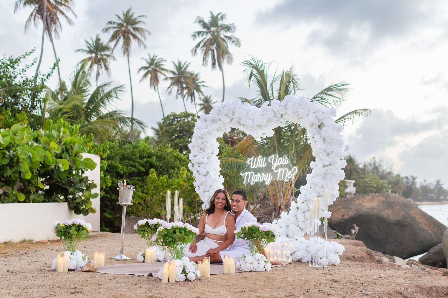 Marriage proposal. Man, woman, and decorative setup with white flower heart overlooking the ocean in Río Grande, Puerto Rico.