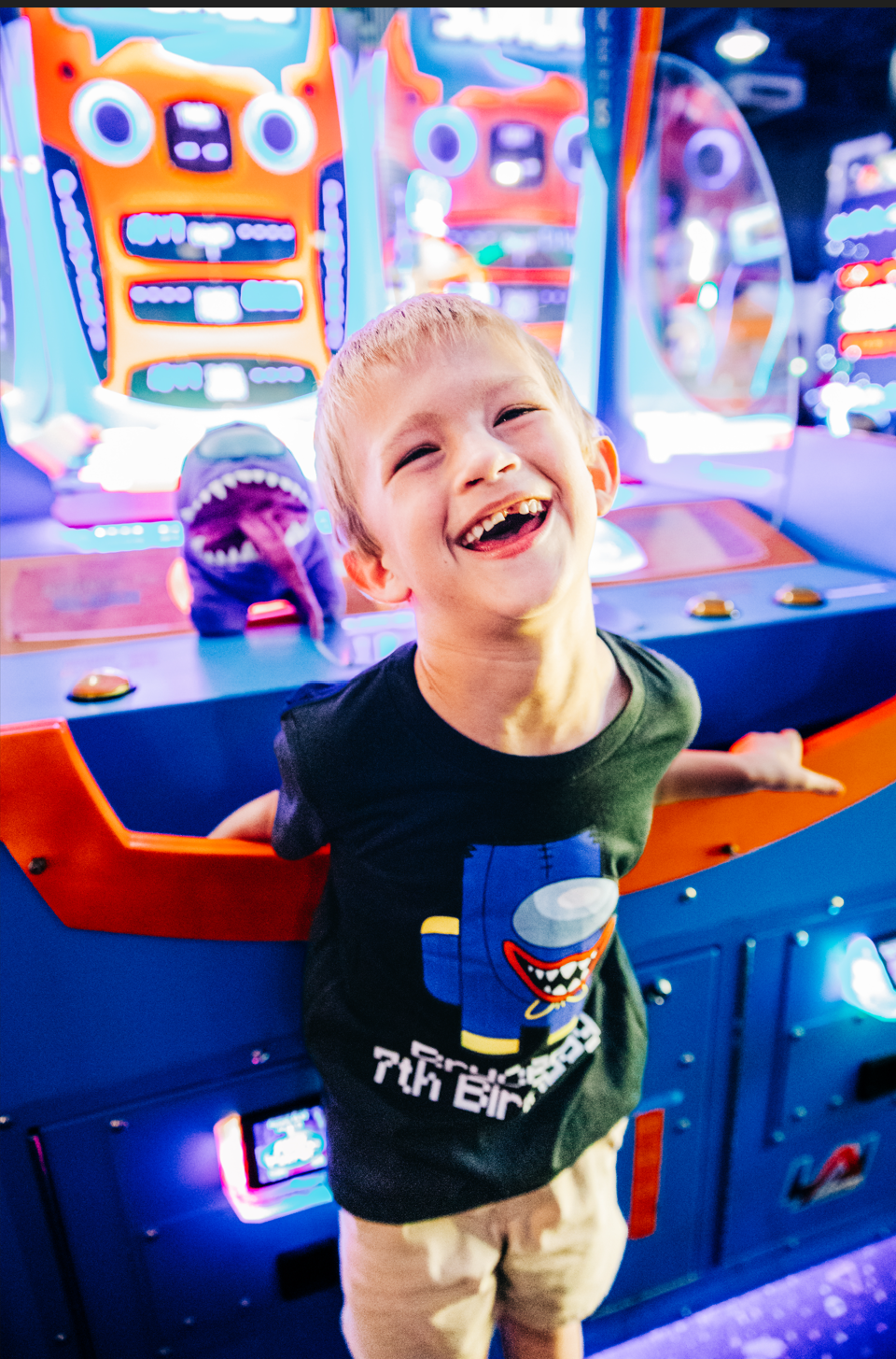 Birthday photos in Lake Worth Beach of a laughing boy surrounded by colorful arcade games at Fun Depot.