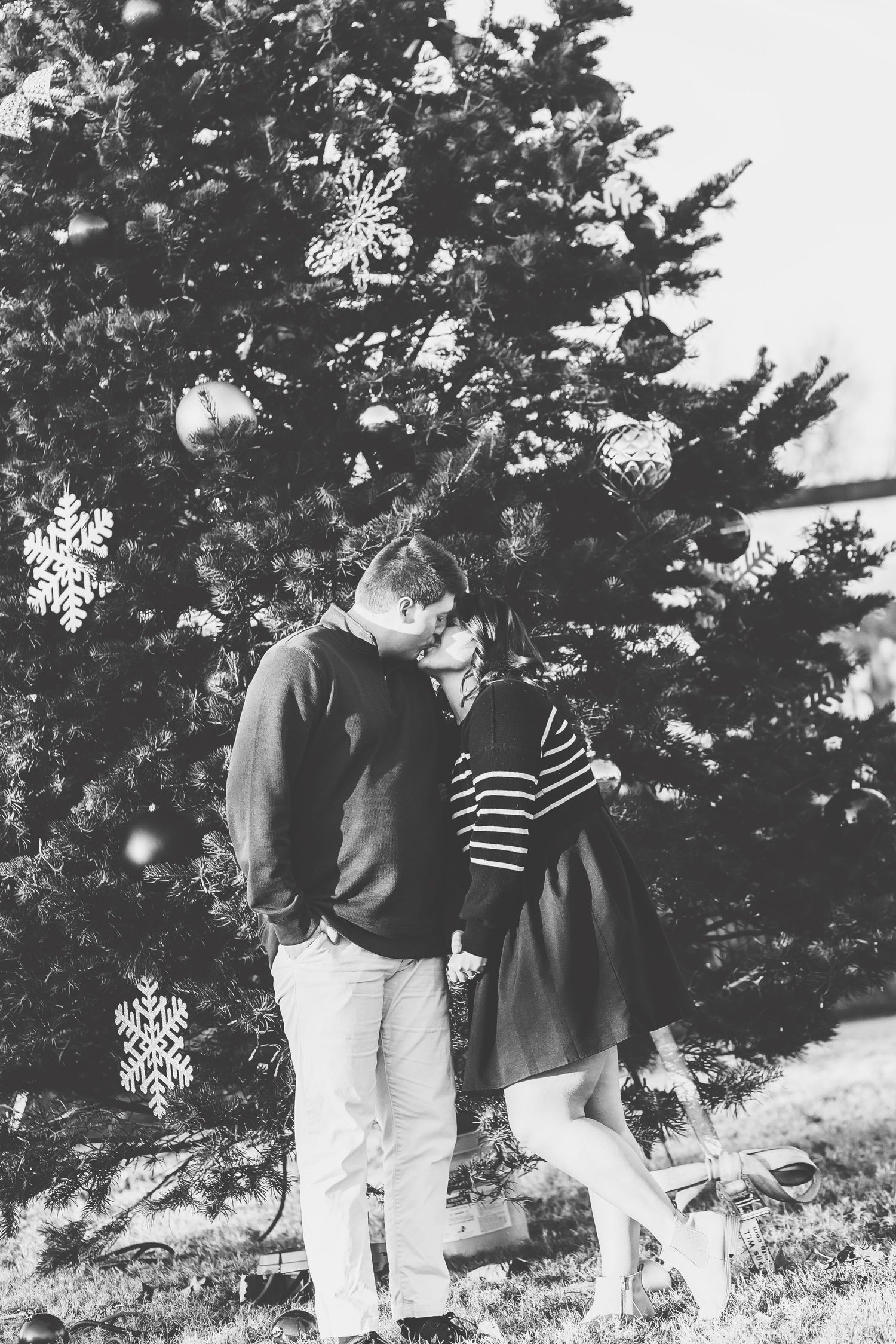 Black and white photo of a happy couple embracing outdoors near evergreen trees.