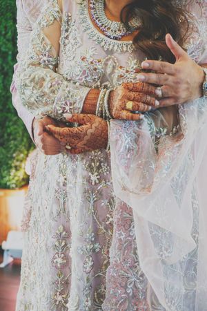 Close-up shots of delicate white lace wedding dress with intricate embroidery and traditional Indian jewelry details.
