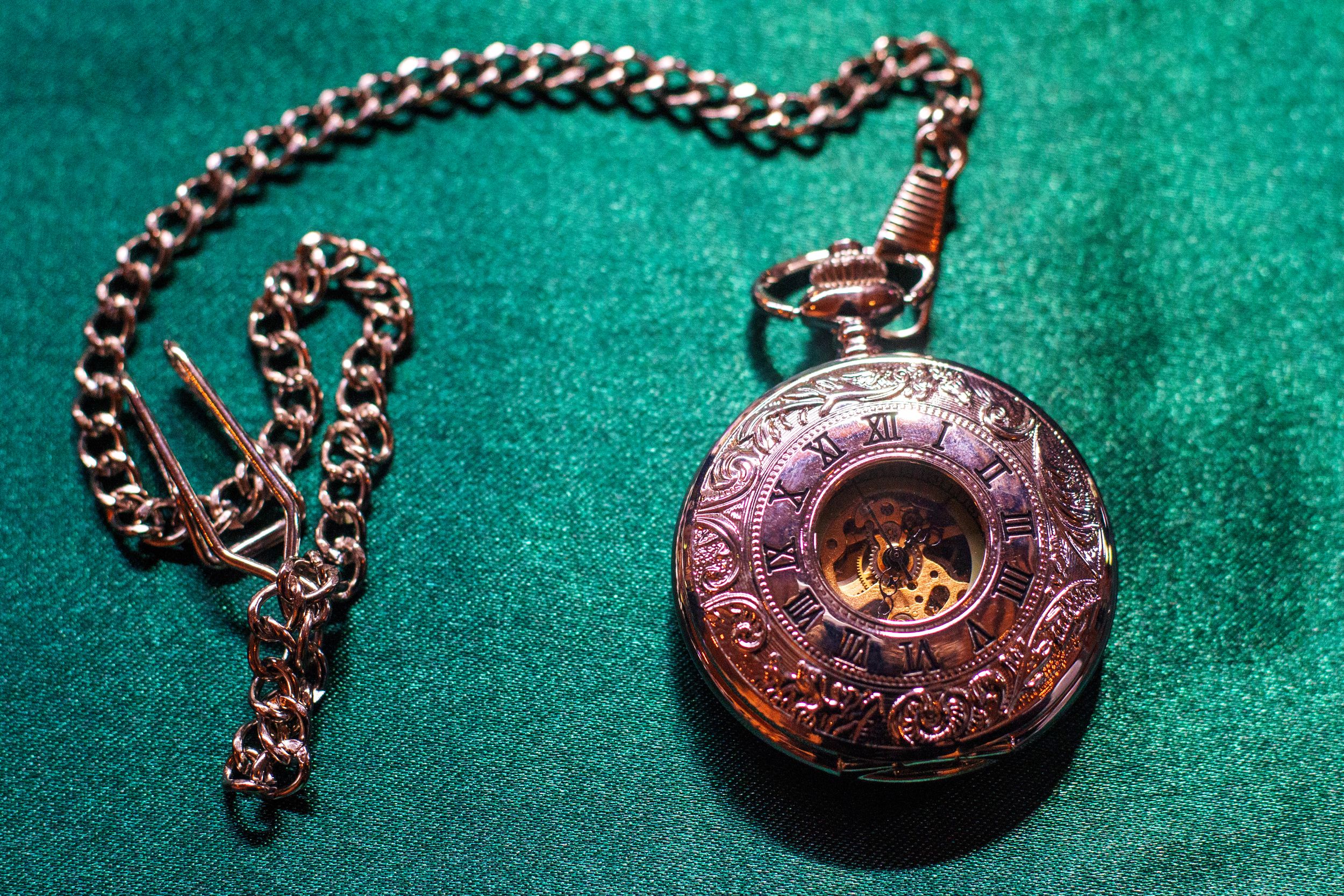 Vintage style pocket watch with ornate details displayed on green velvet surface.