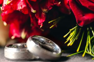Wedding rings photographed with red roses in dramatic lighting.