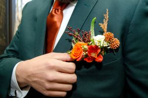 A detailed shot of an autumn-themed boutonniere with orange flowers on a green suit jacket.
