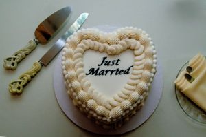 Heart-shaped white wedding cake decorated with piping and 'Just Married' text with serving utensils.