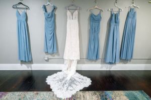 Wedding dress and blue bridesmaid dresses hanging on display against grey wall.
