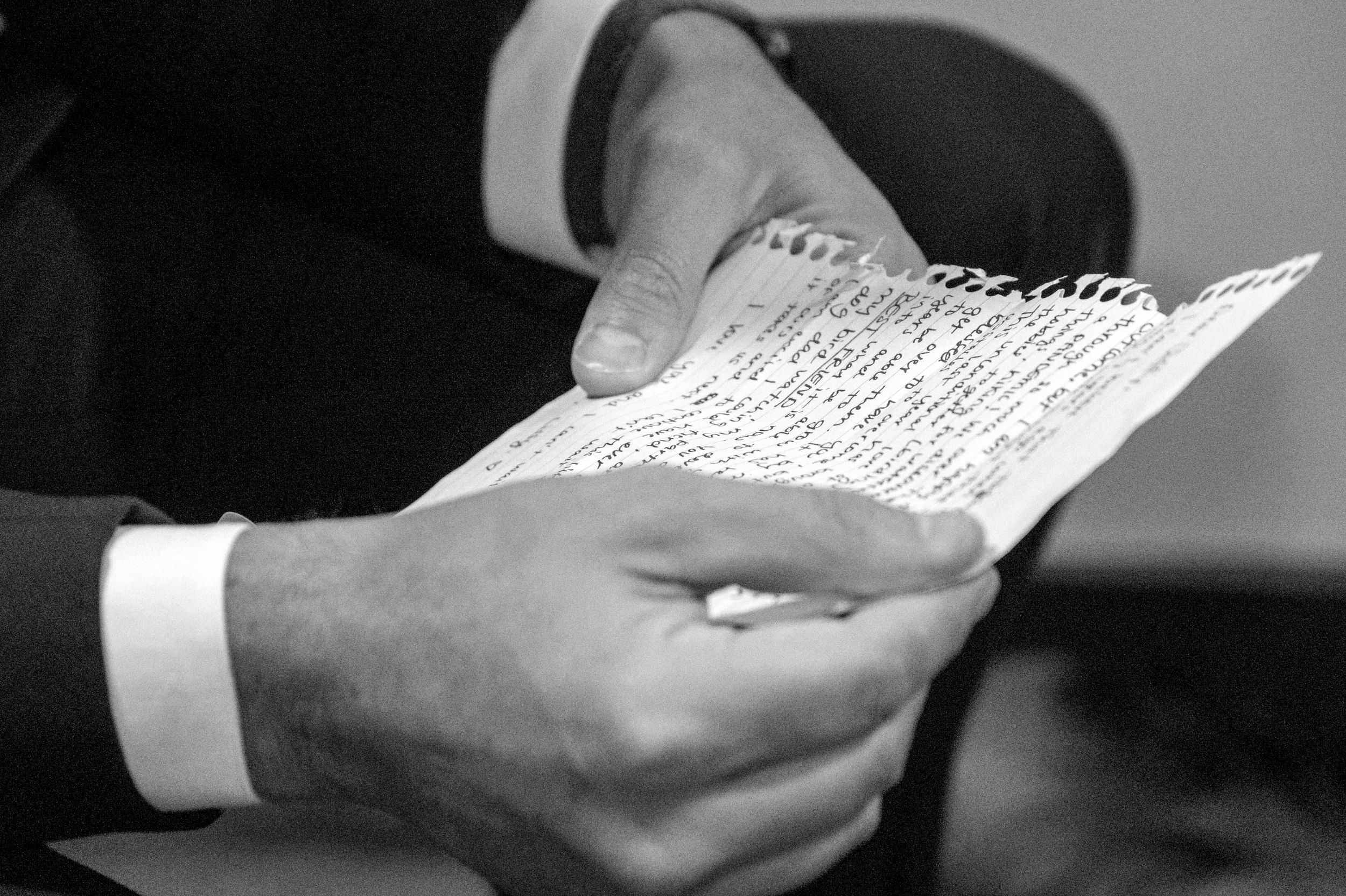 Close-up black and white shot of hands holding handwritten vows during a wedding ceremony.