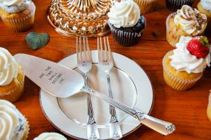 Close-up of wedding cake forks and plate with cupcakes arranged on decorative gold stand.