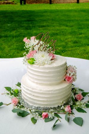 A two-tiered white wedding cake decorated with pink roses and greenery on a white tablecloth.