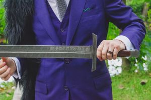 Close-up of hands holding ceremonial sword against purple formal suit.