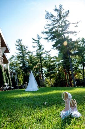 A wedding dress and shoes arranged on sunny lawn with tall pine trees in the background.