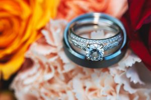 Wedding rings and engagement ring photographed in soft focus with orange and red floral backdrop.
