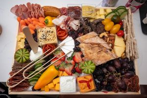 Colorful charcuterie board with assorted meats, cheeses, fruits, and vegetables arranged artistically on wooden surface.