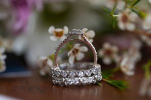 Sparkling diamond wedding rings stacked together with delicate floral blossoms in the background.