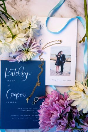 Navy blue wedding invitation suite for Katelyn Kroon and Cooper Purdom with gold jewelry, flowers, and couple photo.