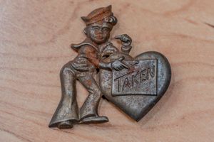 Vintage metal brooch pin featuring a sailor figure leaning on a heart shape with the word TAKEN engraved on it.