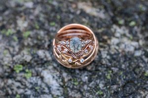 Rose gold ring set with oval moss agate center stone and diamond accents displayed on natural stone surface.